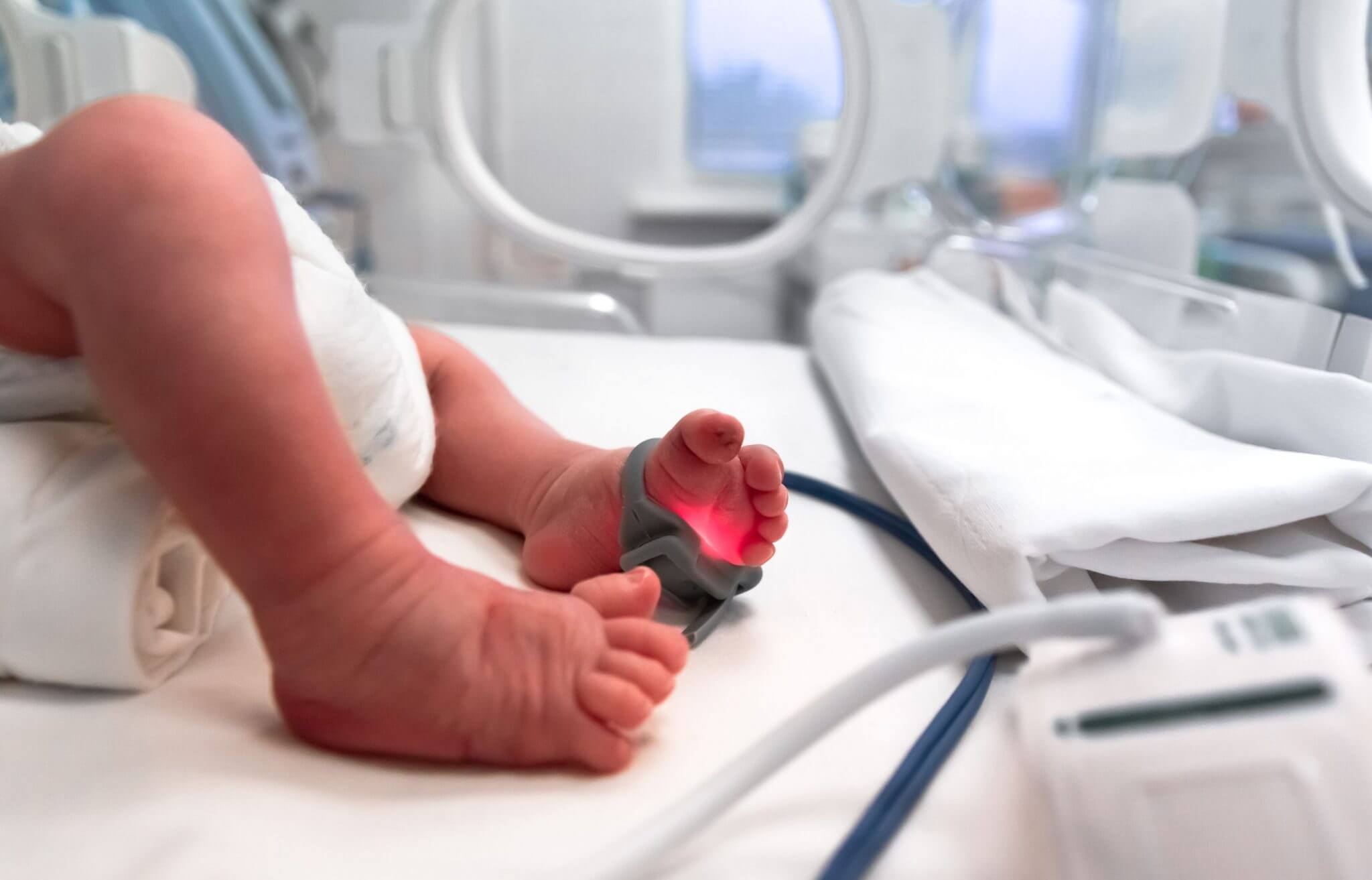 Recém-nascido em berço de hospital com monitoramento neonatal, evidenciando cuidado intensivo à saúde do bebê com foco em monitoramento de sinais vitais.
