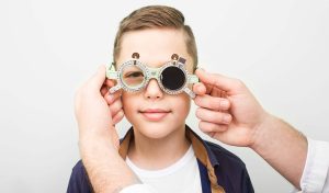 Menino passando pelo exame de vista com óculos oftalmológicos em uma consulta com oftalmologista, enfatizando a importância do cuidado com a saúde ocular infantil.