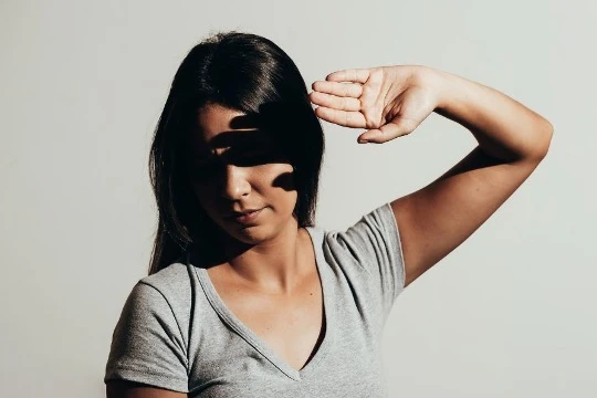 Mulher com uma camiseta cinza criando sombras com a mão, representando conceitos de luz e forma na fotografia.