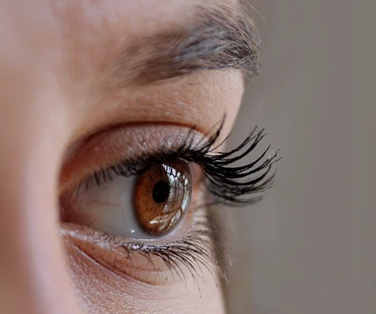 Close-up de um olho castanho com cílios longos, destacando a beleza e os detalhes da íris. A imagem captura a atenção ao mostrar a profundidade do olhar.