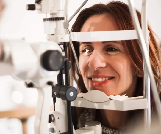 Mulher sorrindo durante exame de vista em consultório oftalmológico. Equipamento óptico em foco. Importância da saúde ocular.